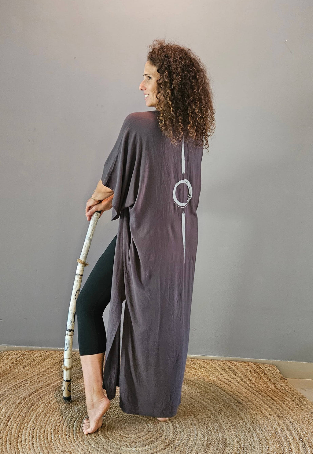 Woman in a long, dark-grey kimono standing on a textured rug with a plain wall behind her.