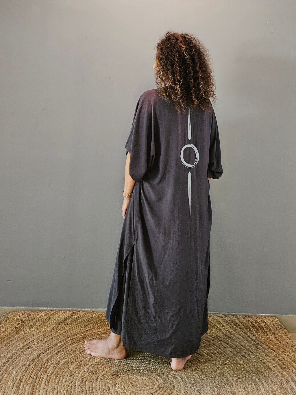 Person wearing a long dark grey kimono standing in front of a plain wall.