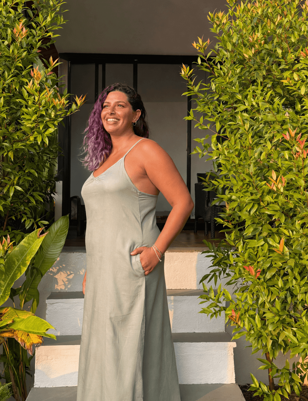 Woman in a jade dress standing in front of a mirror with reflections and greenery.