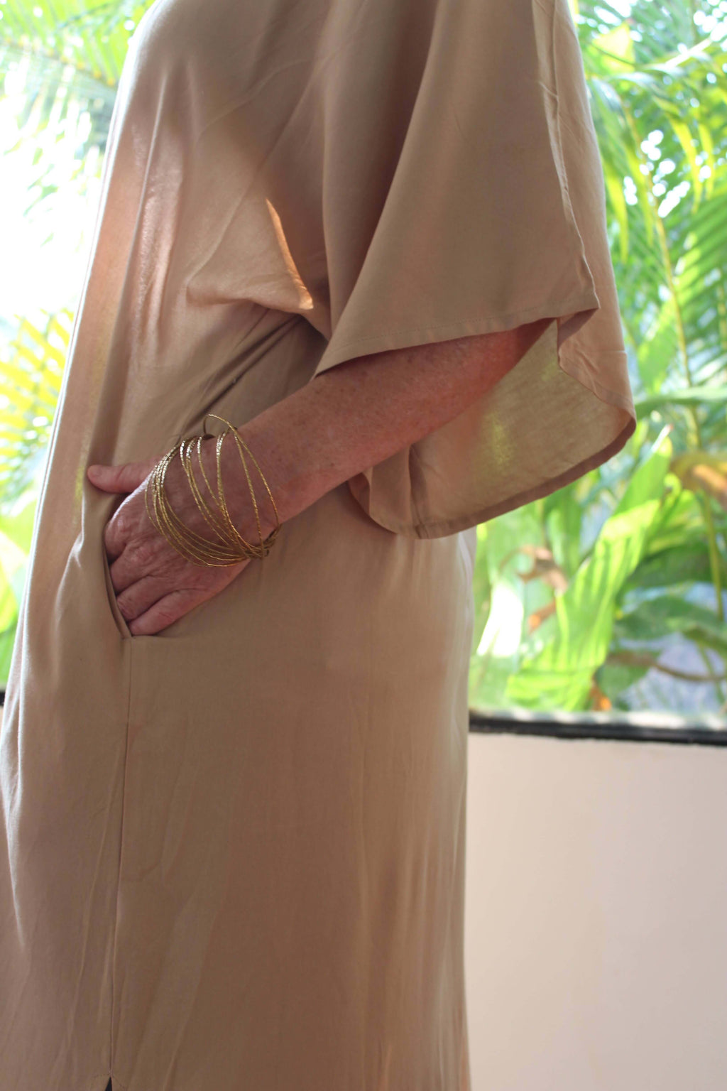 Person wearing a sand long kimono with pockets with a blurred background of greenery