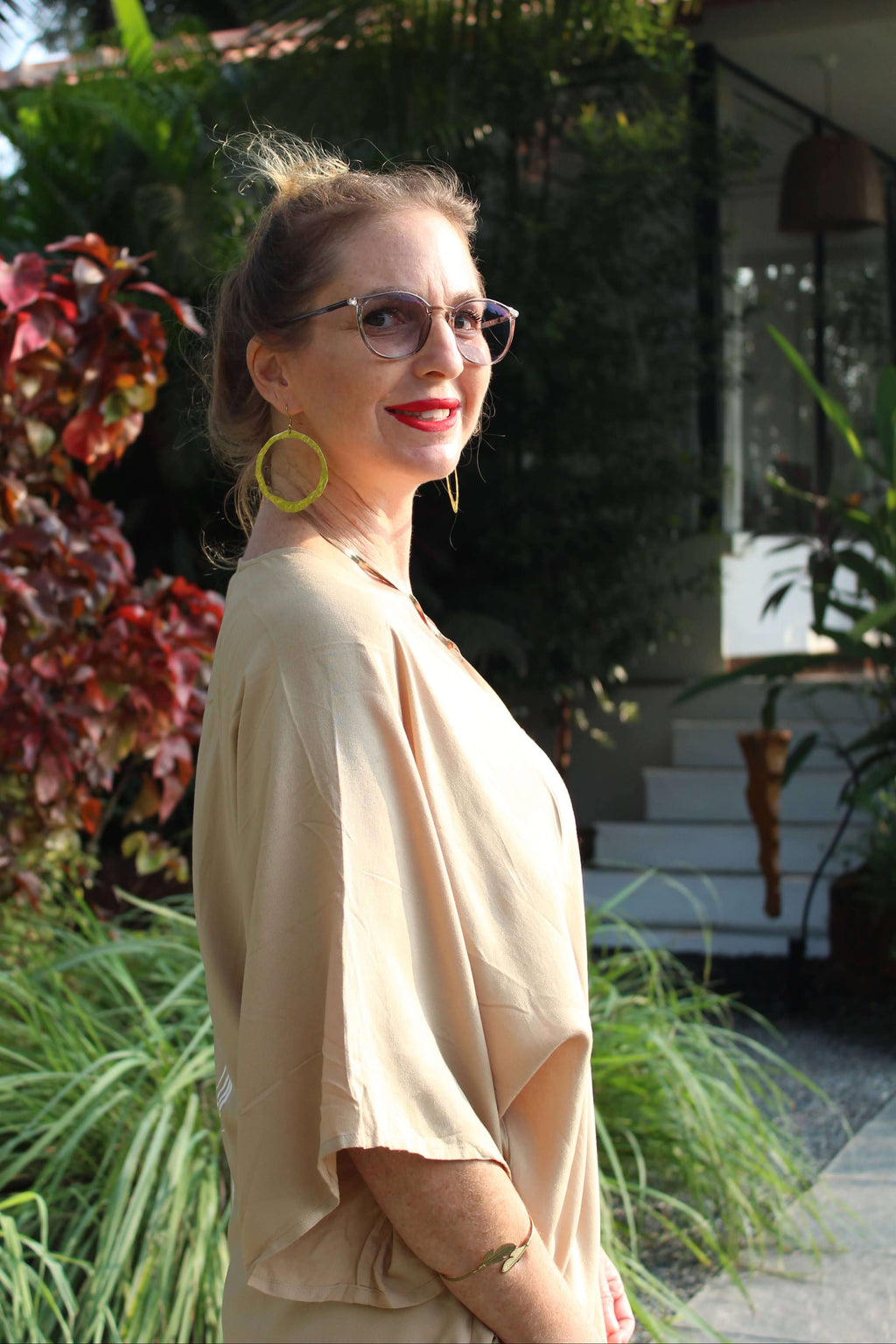 Woman wearing a sand long kimono outdoors with greenery and a building in the background