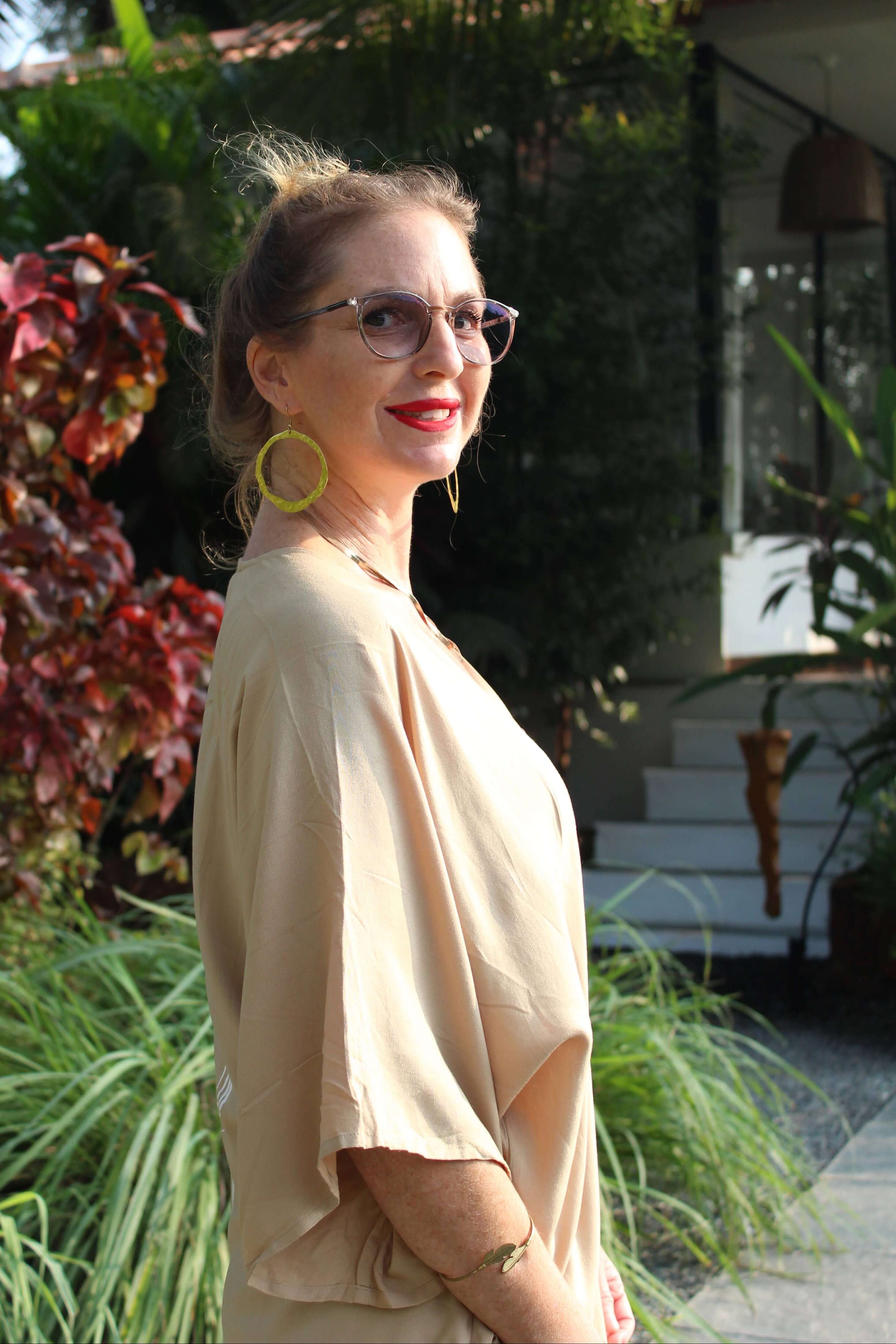 Woman wearing a sand long kimono outdoors with greenery and a building in the background