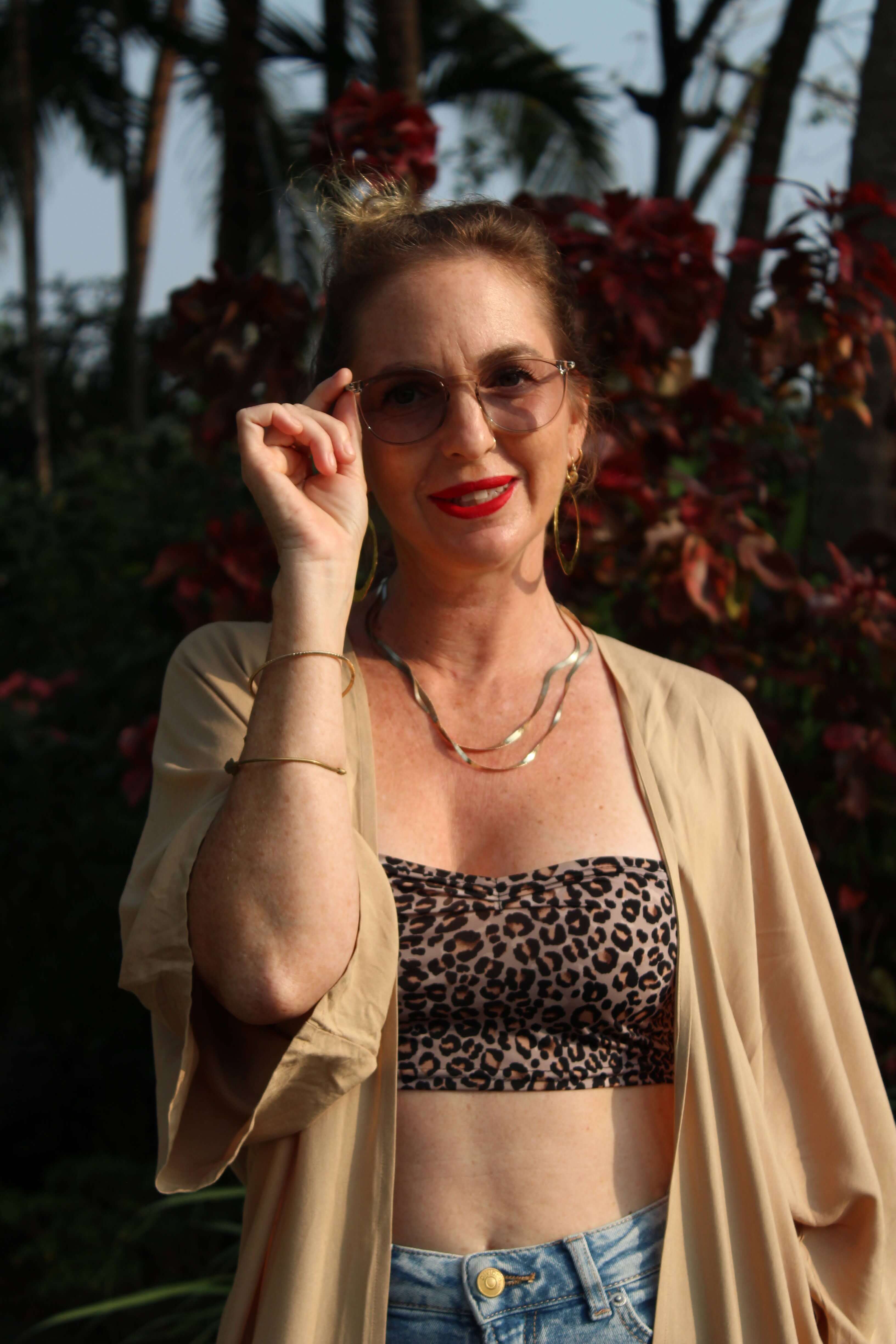 Woman wearing a leopard print top and sand long kimono with sunglasses, standing outdoors.