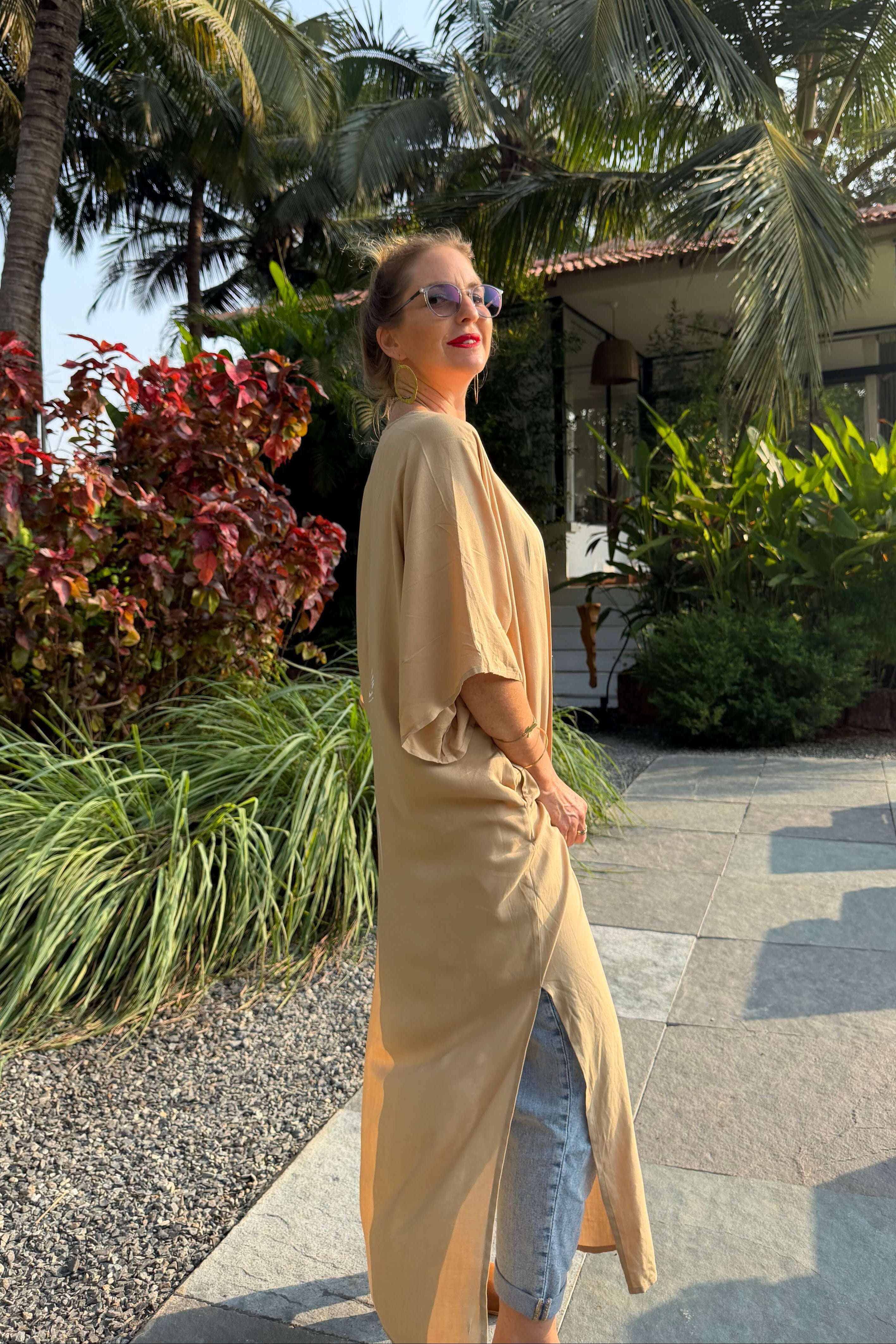 Woman in a sand long kimono standing outdoors with palm trees and plants in the background