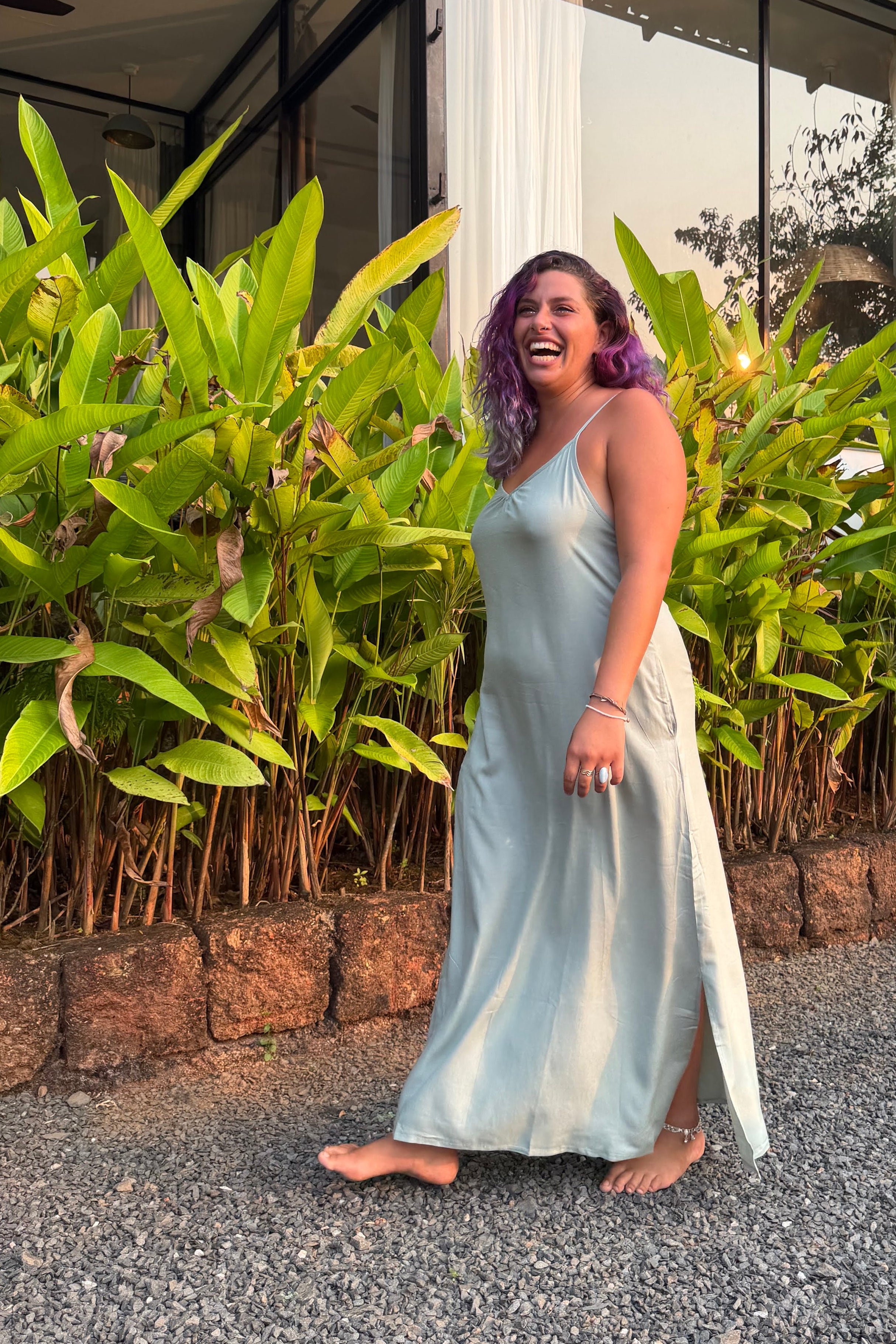 Person in a jade dress standing on a road with plants and a building in the background
