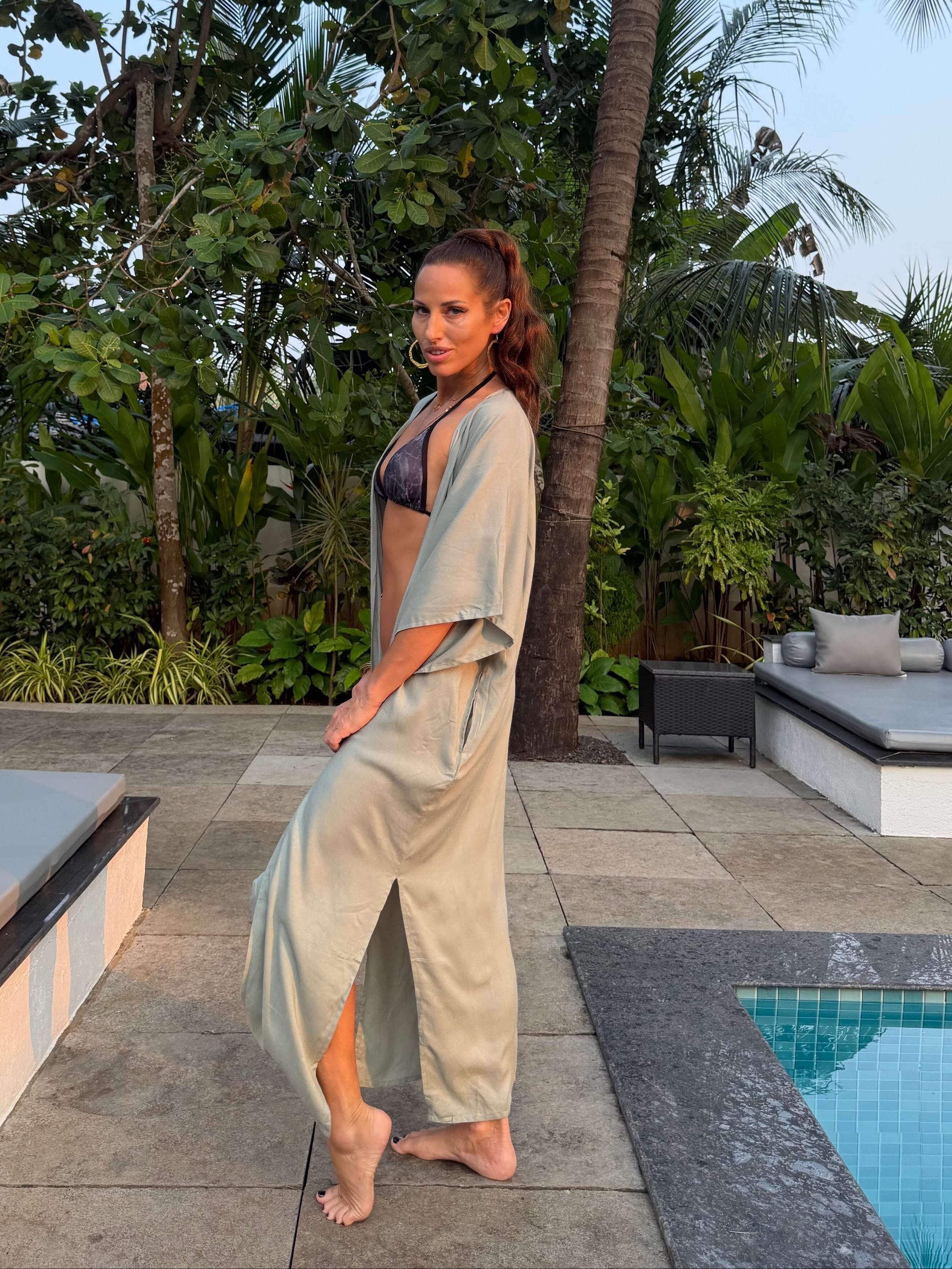 Woman in a swimsuit and kimono standing by a pool with palm trees in the background