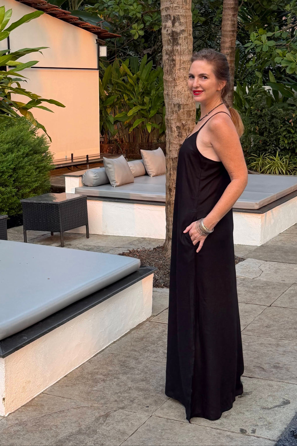 Woman in a black dress standing outdoors with palm trees and modern architecture in the background
