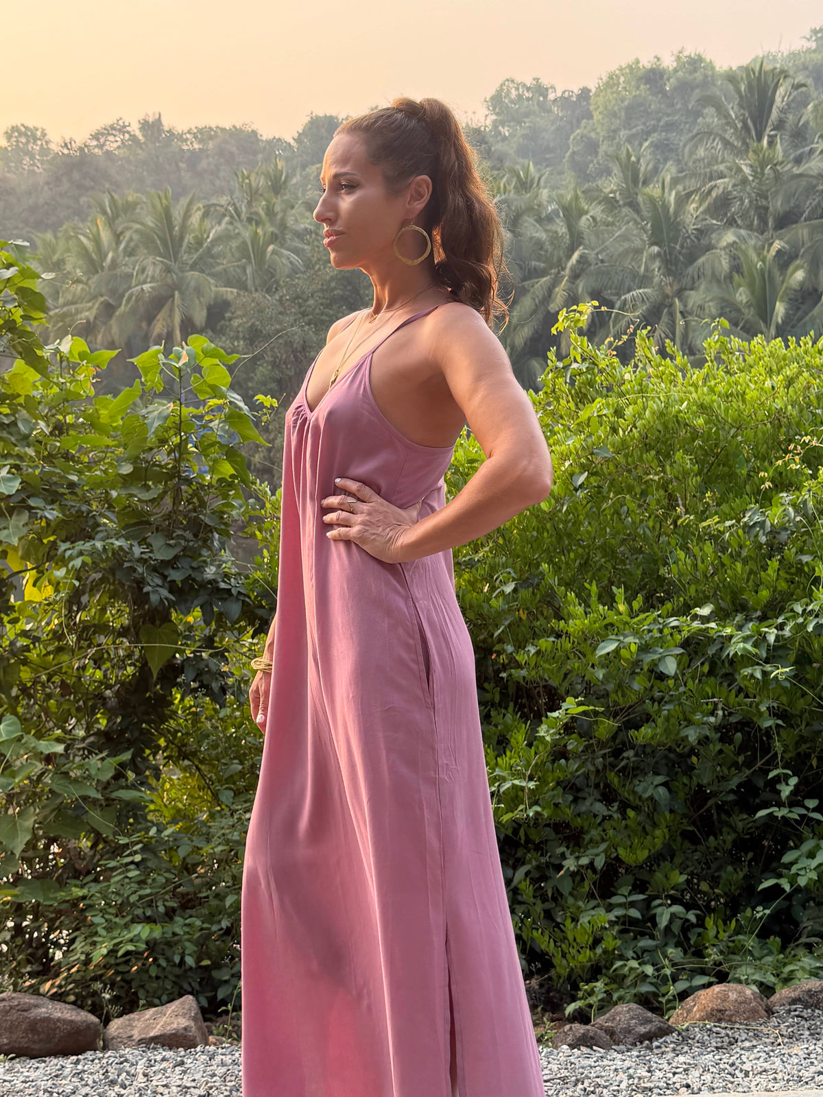 Woman in a pink dress standing outdoors with greenery in the background
