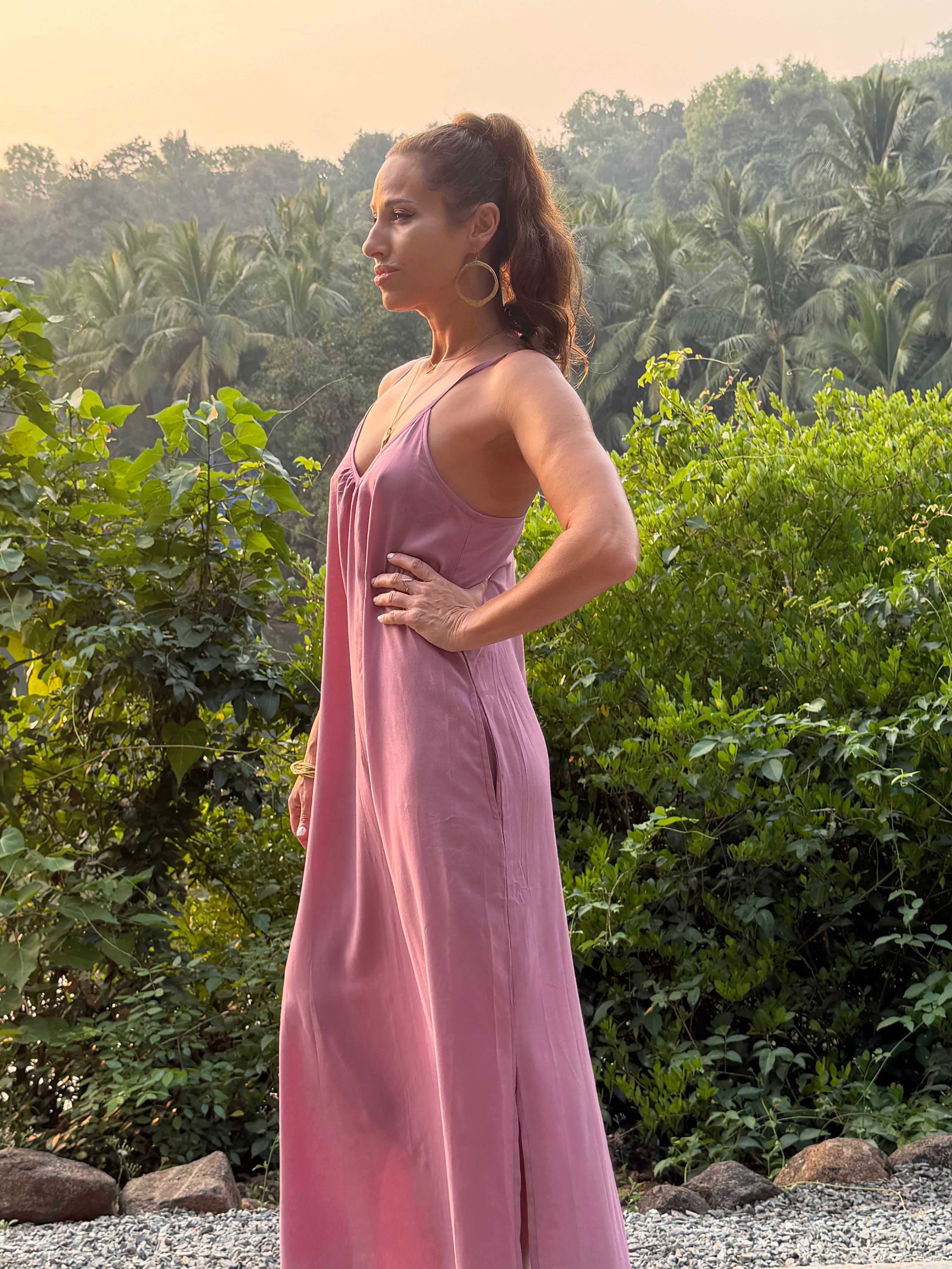 Woman in a pink dress standing outdoors with greenery in the background