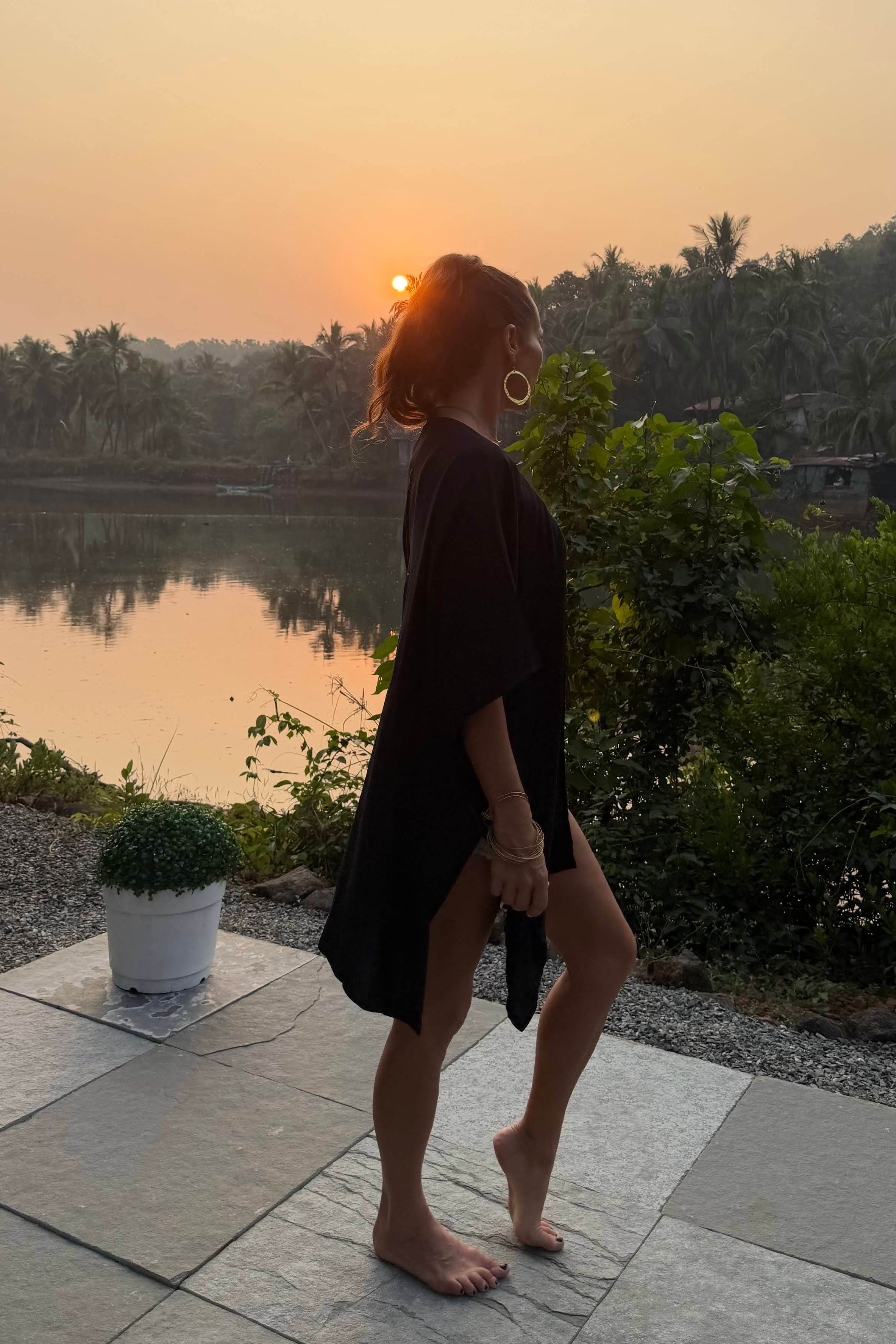 Woman standing by a river at sunset wearing a black kimono with trees in the background